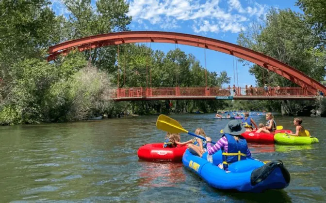 Rafts and tubes floating the Boise River under a red arched footbridge