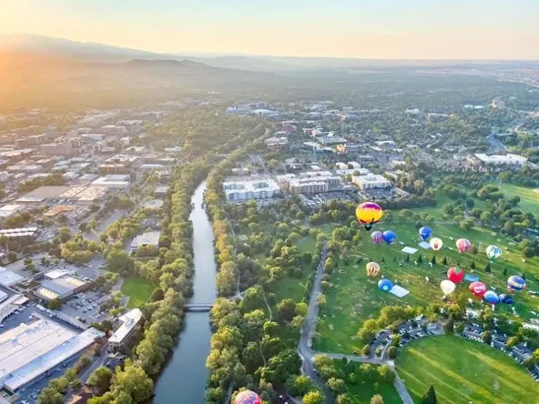 Aerial view of the Boise River winding through downtown, with hot-air balloons over Ann Morrison Park